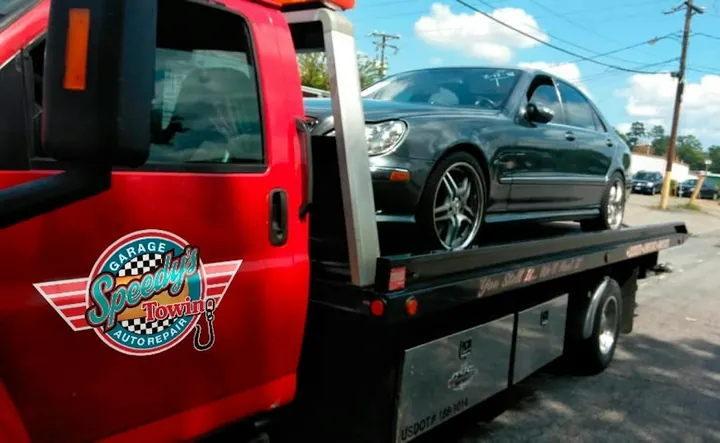 A Speedy's flatbed tow truck carrying a gray car